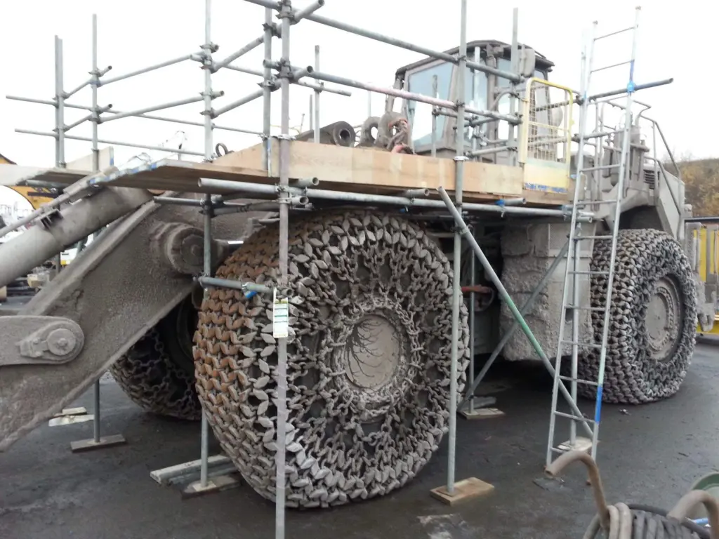 large industrial wheel loader, likely a Cat 992, which has scaffolding erected around its massive wheels for maintenance or inspection.